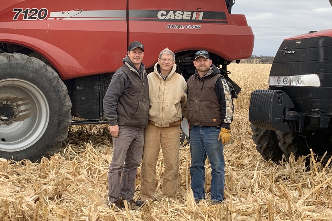 Chris Pearson, his father and brother pose for a picture in front of a red tractor.